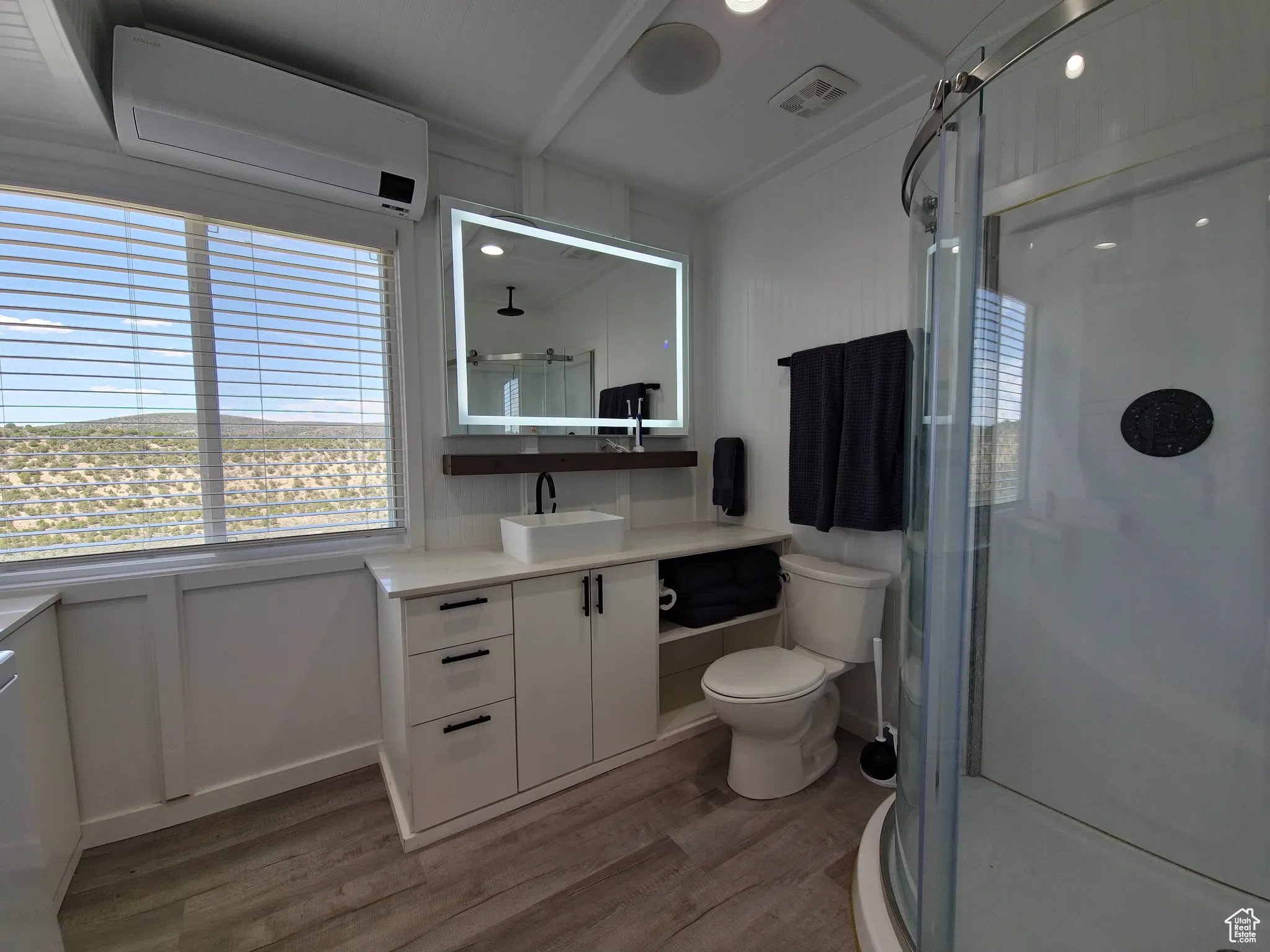 Bathroom with an AC wall unit, wood finished floors, vanity, a stall shower, and a decorative wall