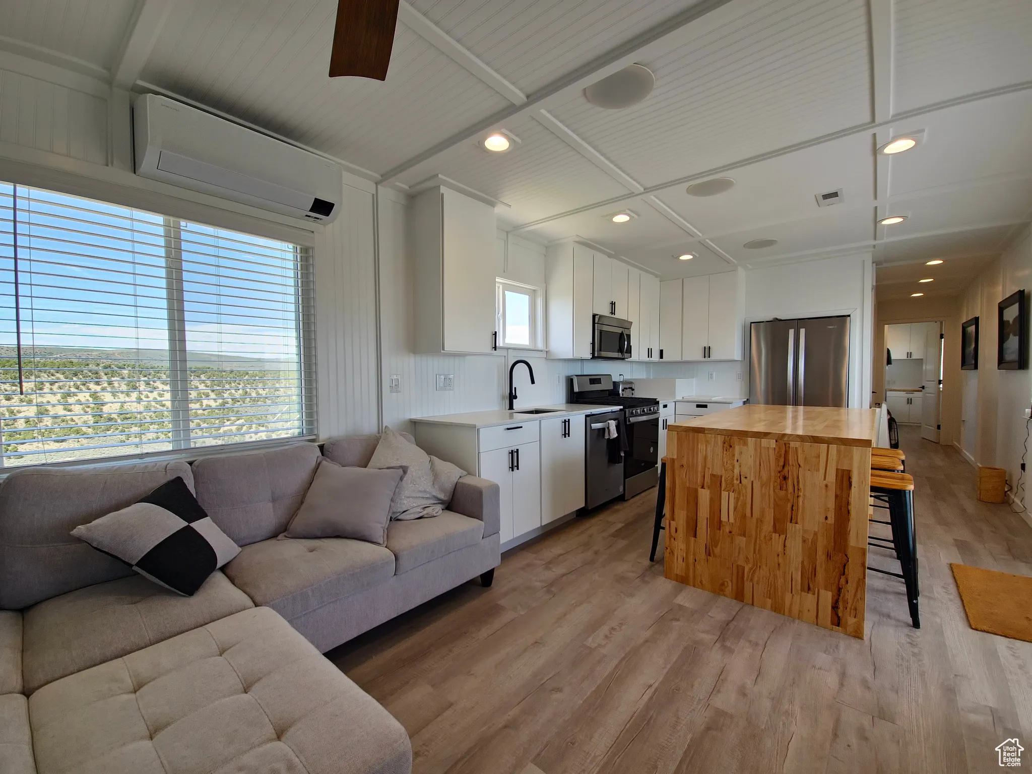 Kitchen with stainless steel appliances, open floor plan, a kitchen bar, an AC wall unit, and light wood-style flooring