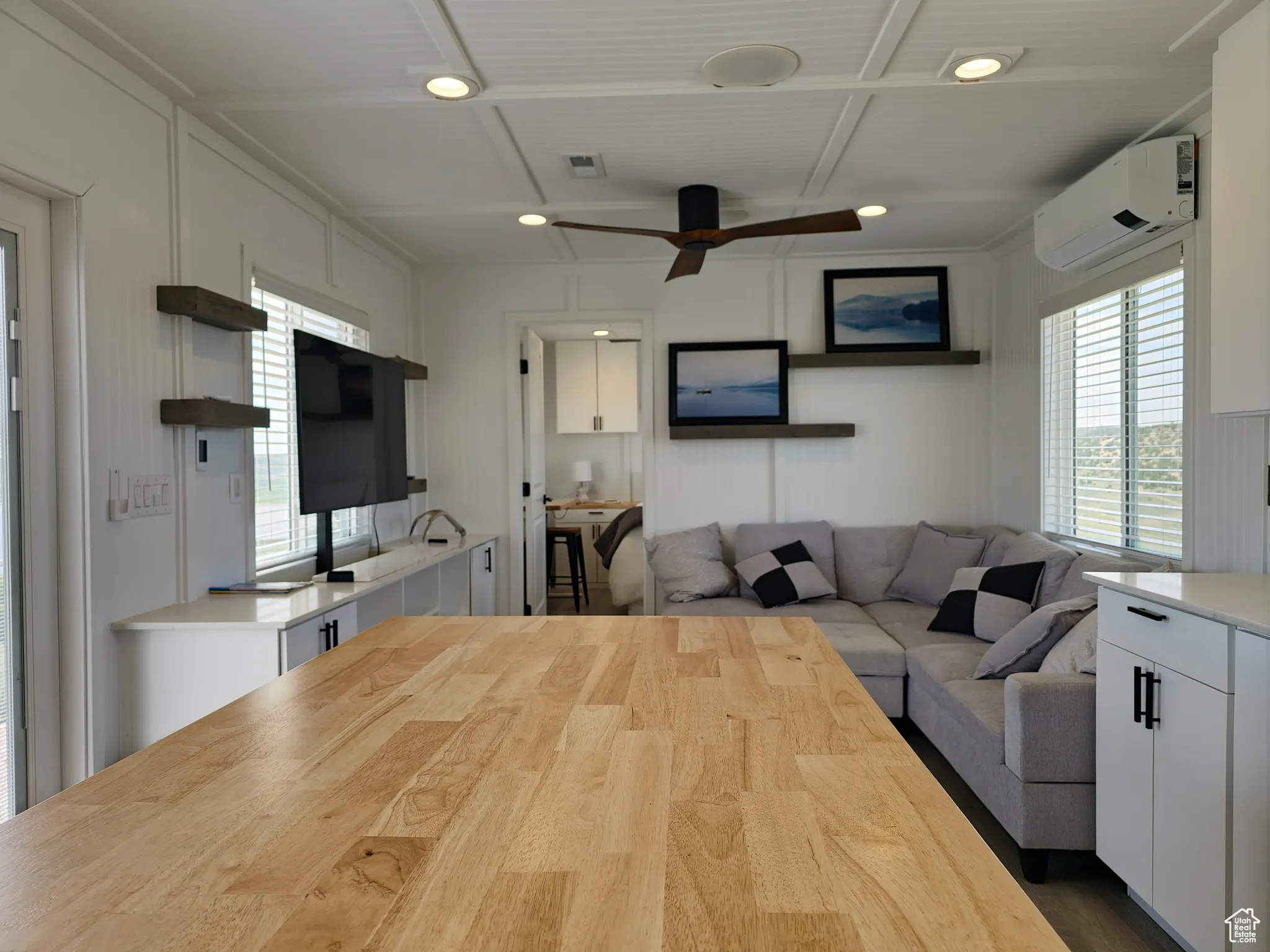 Living area featuring a wall mounted air conditioner, ceiling fan, a decorative wall, coffered ceiling, and dark wood finished floors