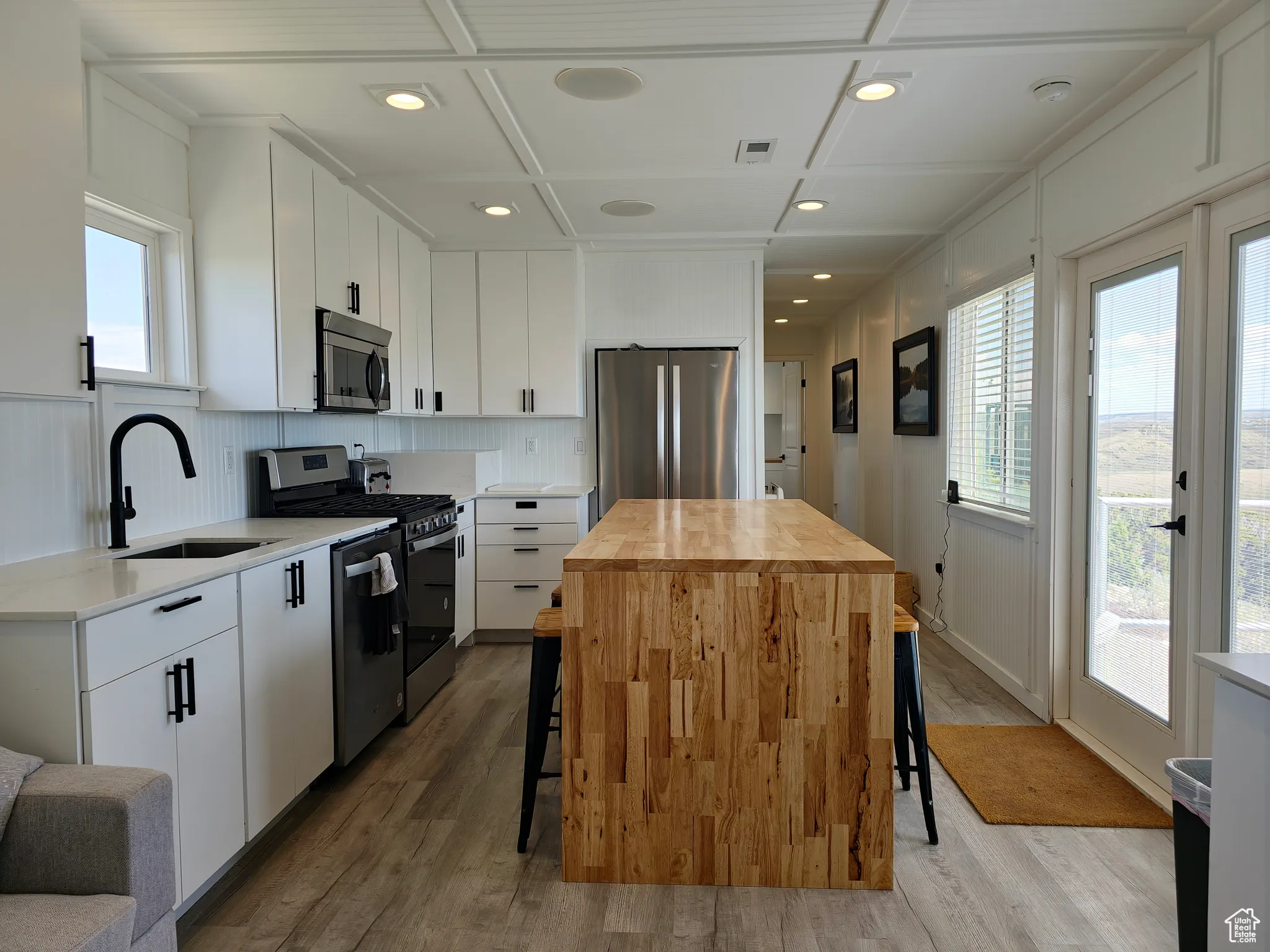 Kitchen featuring stainless steel appliances, butcher block counters, coffered ceiling, light wood finished floors, and a kitchen breakfast bar