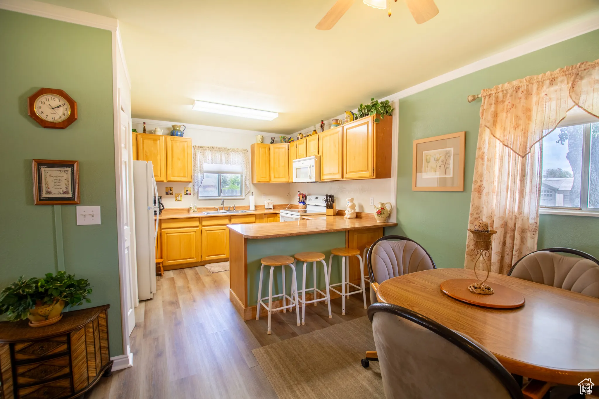 Kitchen with white appliances, light brown cabinets, a peninsula, a breakfast bar, and light wood-style floors