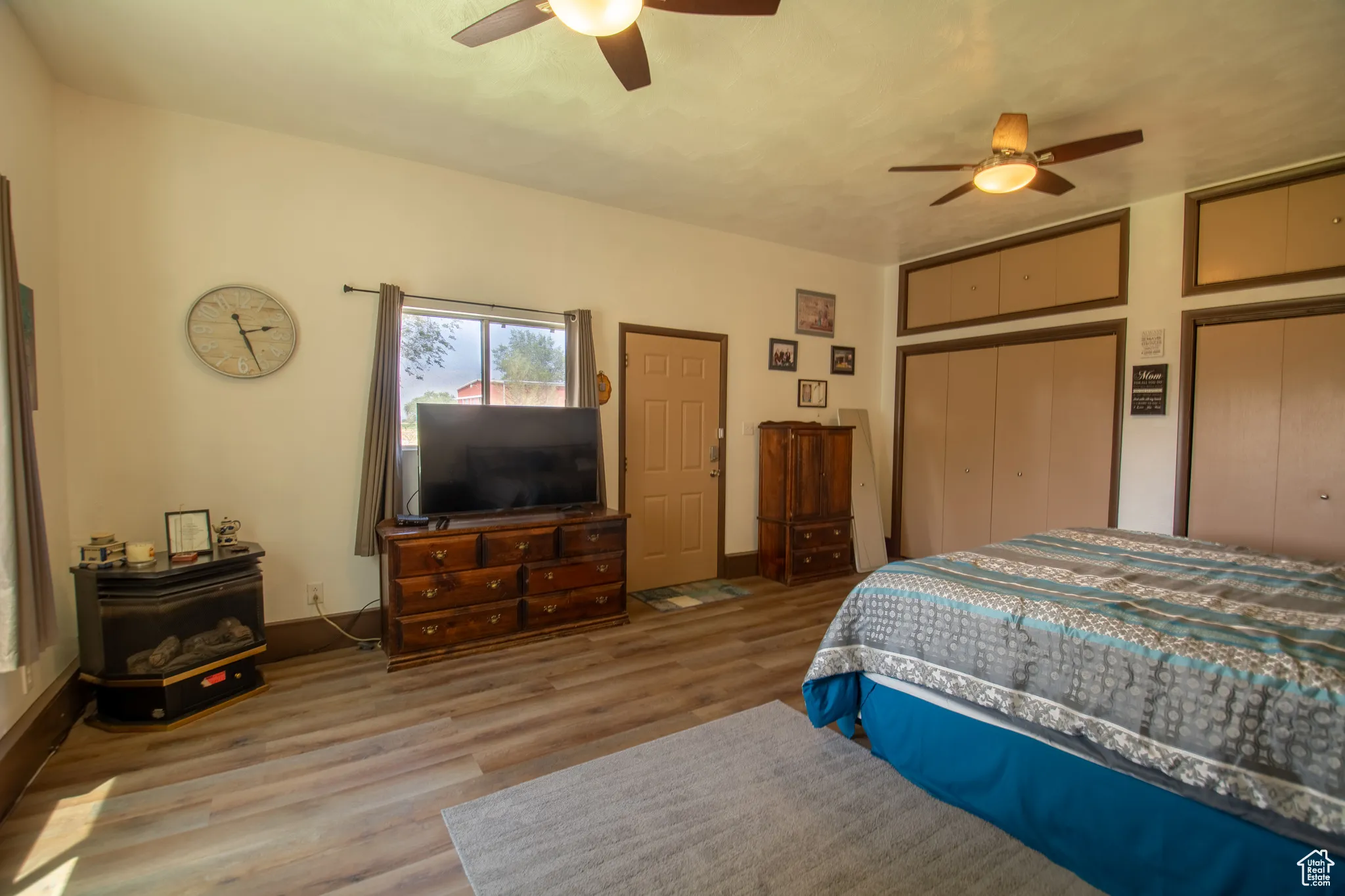 Bedroom with a wood stove, wood finished floors, a ceiling fan, and two closets