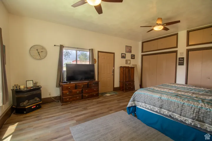 Bedroom with a wood stove, wood finished floors, a ceiling fan, and two closets