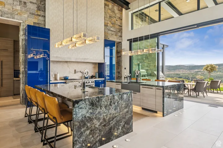 Kitchen with modern cabinets, a towering ceiling, a mountain view, dark stone counters, and a kitchen island with sink