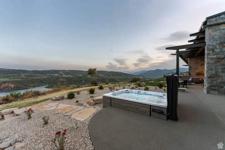 Pool at dusk with a hot tub, a patio, and a water and mountain view