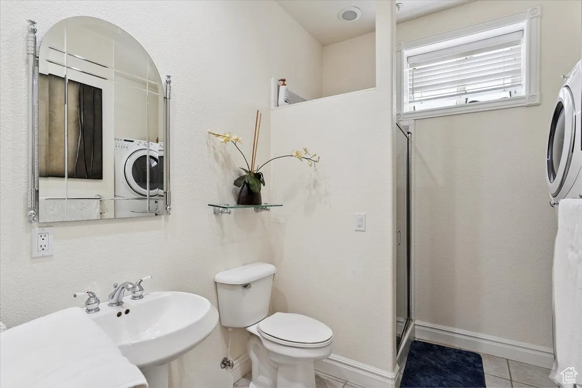 Full bath with tile patterned floors, an enclosed shower, and washer / dryer