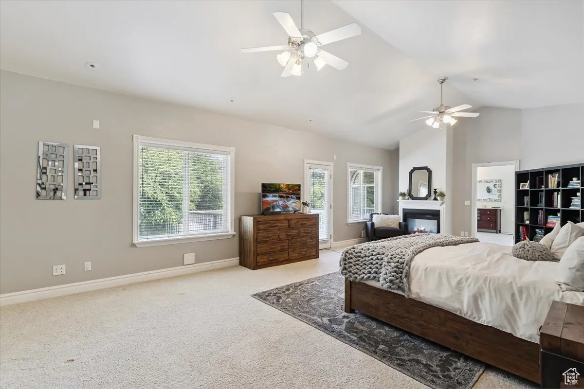 Carpeted bedroom with a glass covered fireplace, lofted ceiling, and a ceiling fan