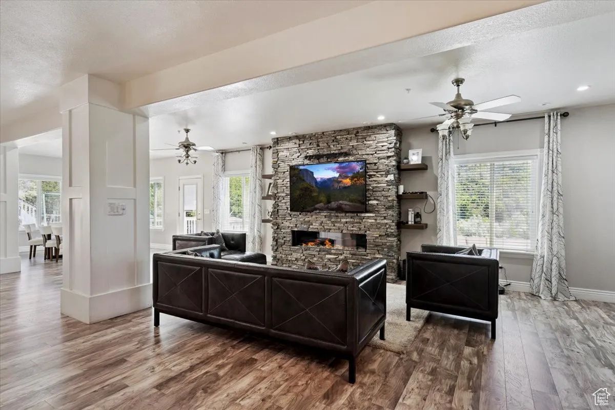 Living area featuring a ceiling fan, wood finished floors, a fireplace, a textured ceiling, and recessed lighting