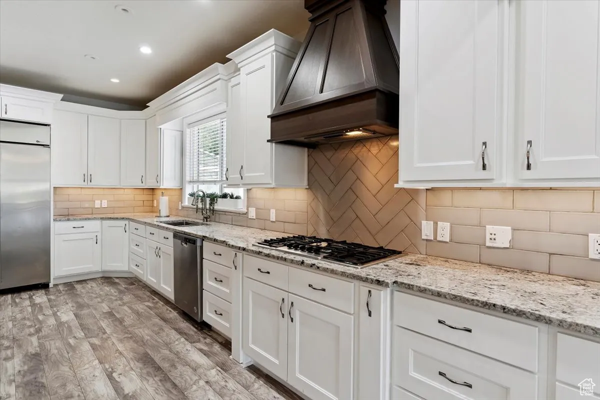 Kitchen with appliances with stainless steel finishes, premium range hood, white cabinets, and recessed lighting