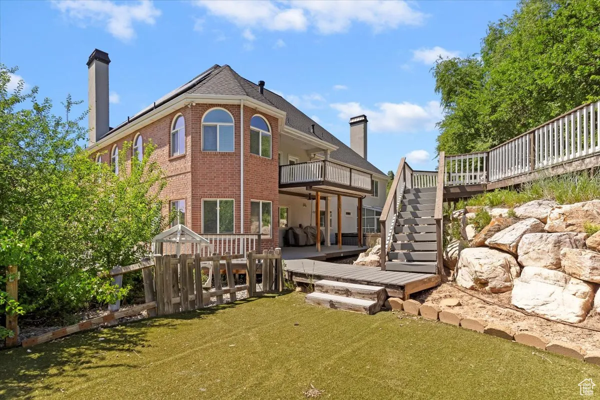Rear view of house with brick siding, stairway, a deck, a chimney, and a yard