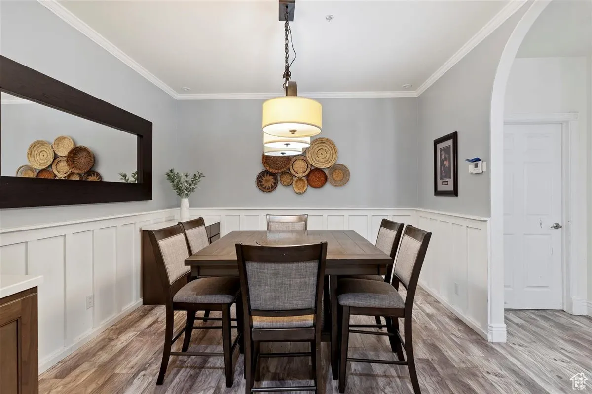 Dining room featuring light wood-style floors, arched walkways, crown molding, wainscoting, and a decorative wall