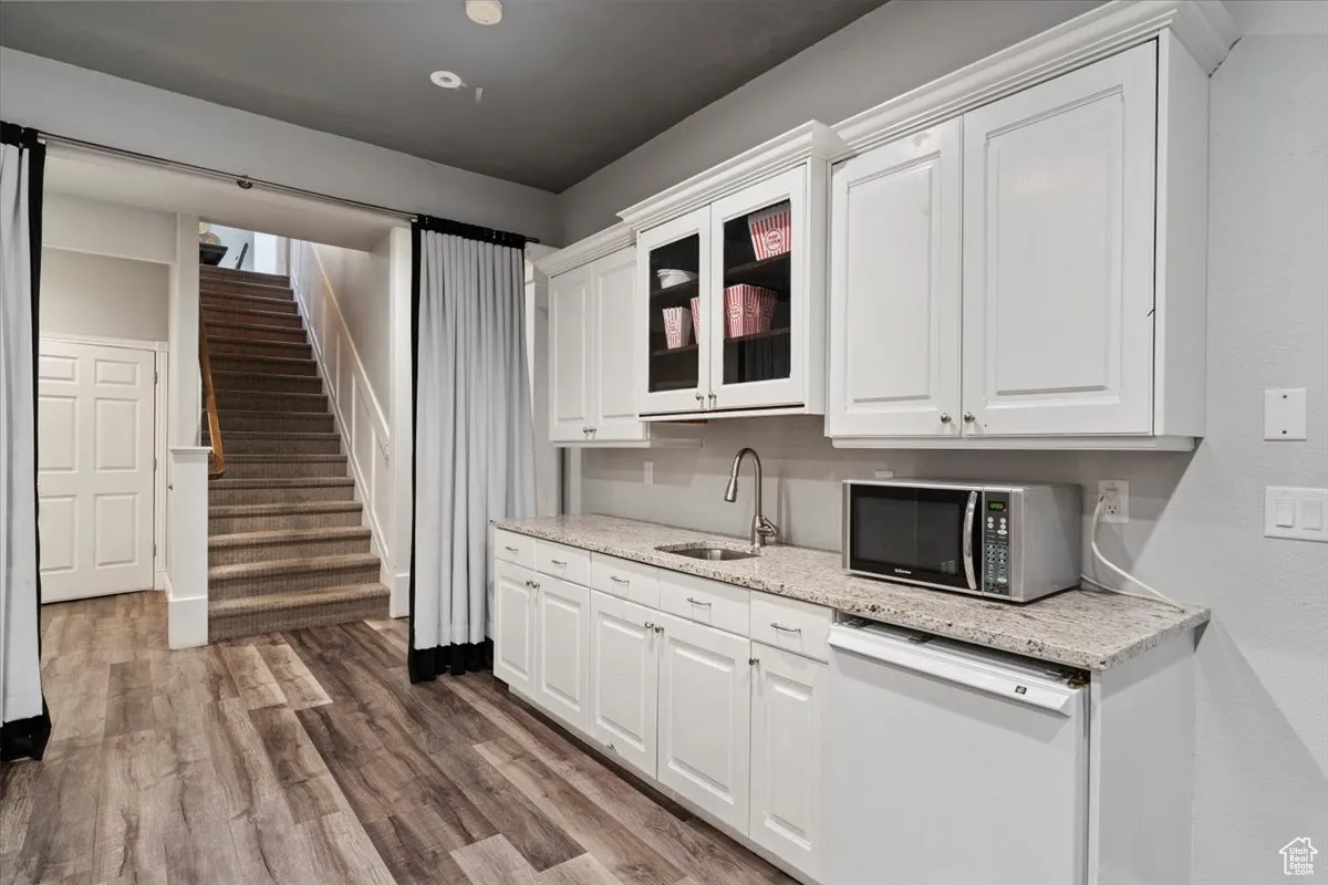 Kitchen with white dishwasher, white cabinets, wood finished floors, and glass insert cabinets