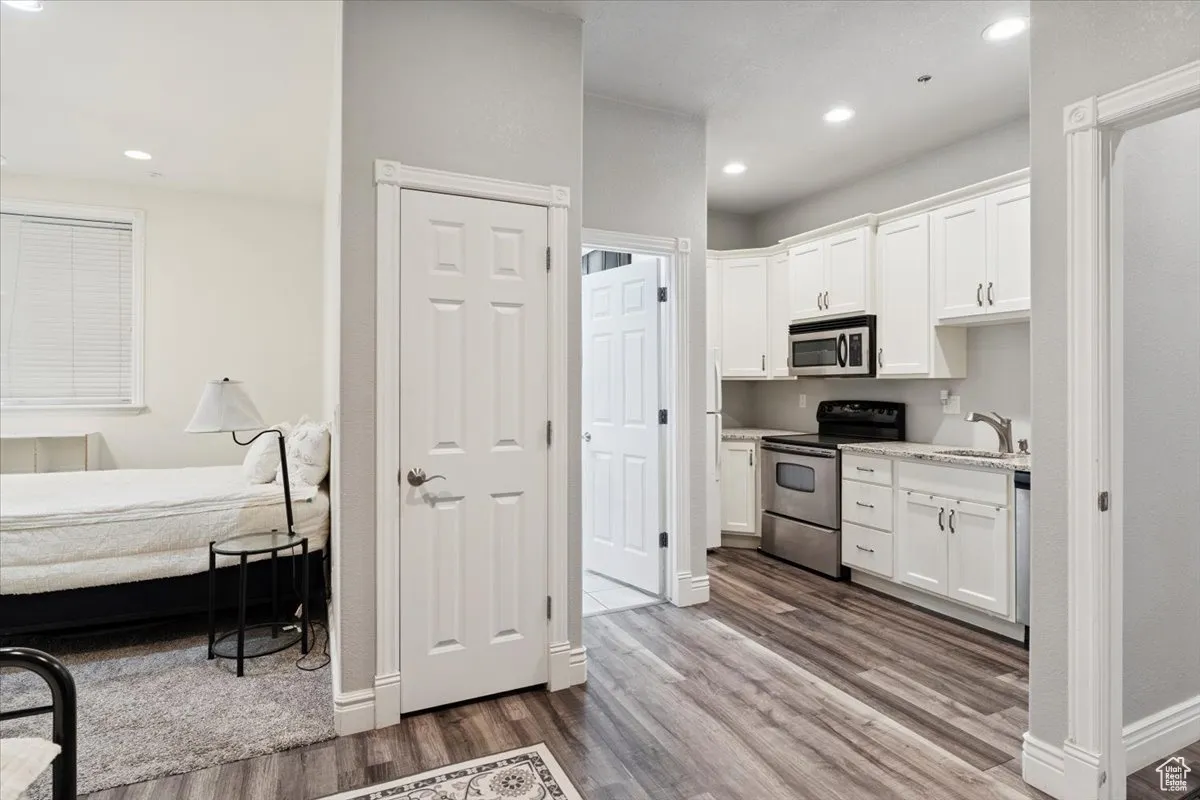 Kitchen with stainless steel appliances, wood finished floors, white cabinetry, and recessed lighting