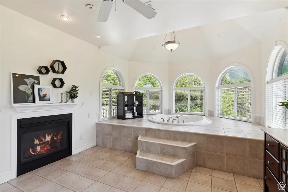 Bathroom with a bath, healthy amount of natural light, a glass covered fireplace, tile patterned floors, and a towering ceiling