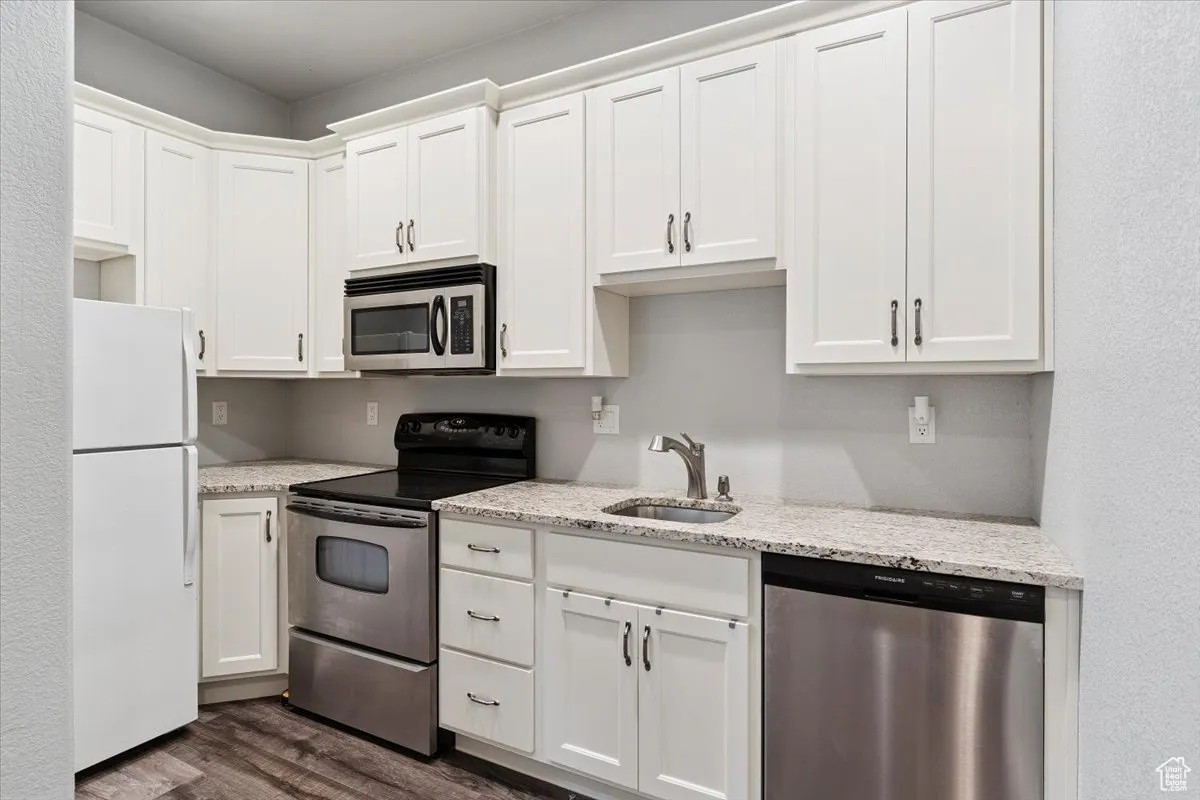 Kitchen with appliances with stainless steel finishes, dark wood-style flooring, and white cabinetry