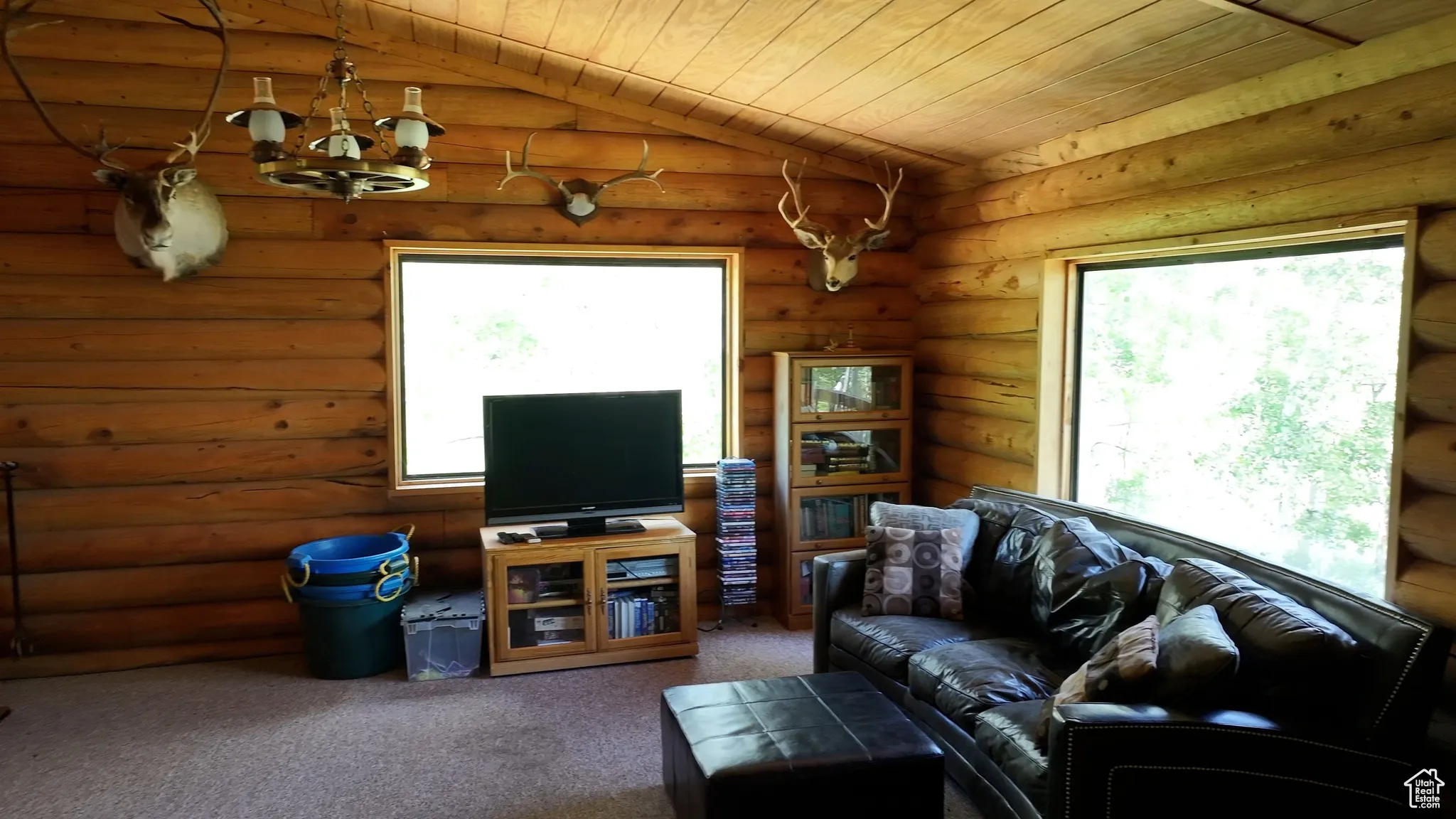 Carpeted living area with vaulted ceiling, wood ceiling, a chandelier, and rustic walls