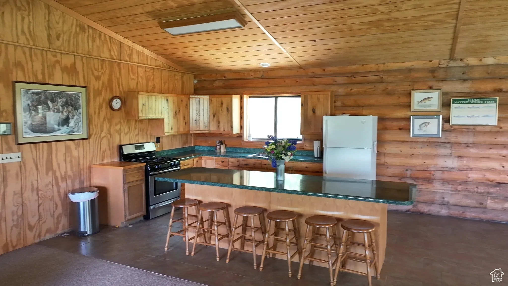 Kitchen featuring freestanding refrigerator, stainless steel gas range, wood ceiling, log walls, and a kitchen breakfast bar
