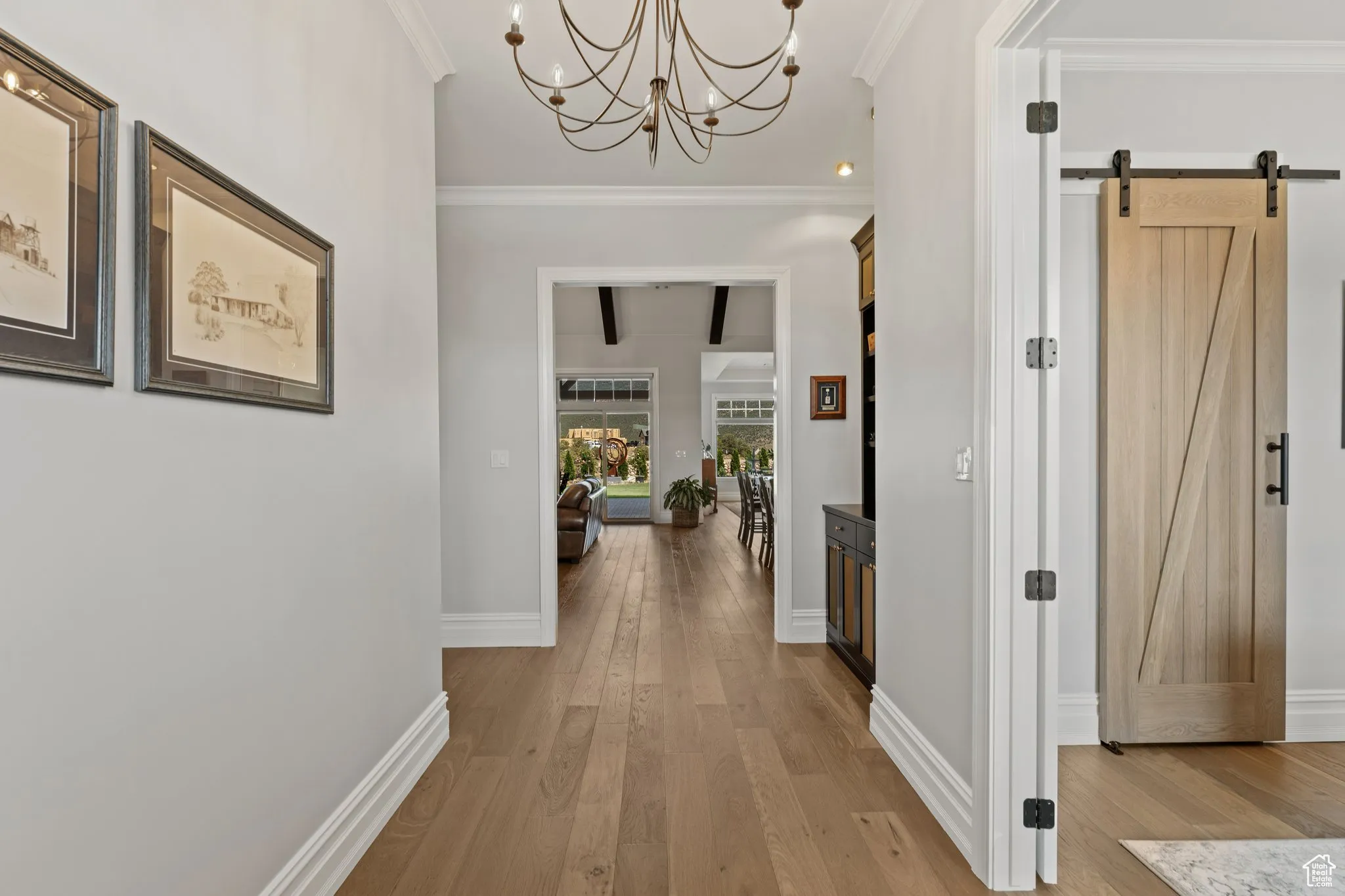 Corridor with a barn door, light wood-style flooring, ornamental molding, and a chandelier