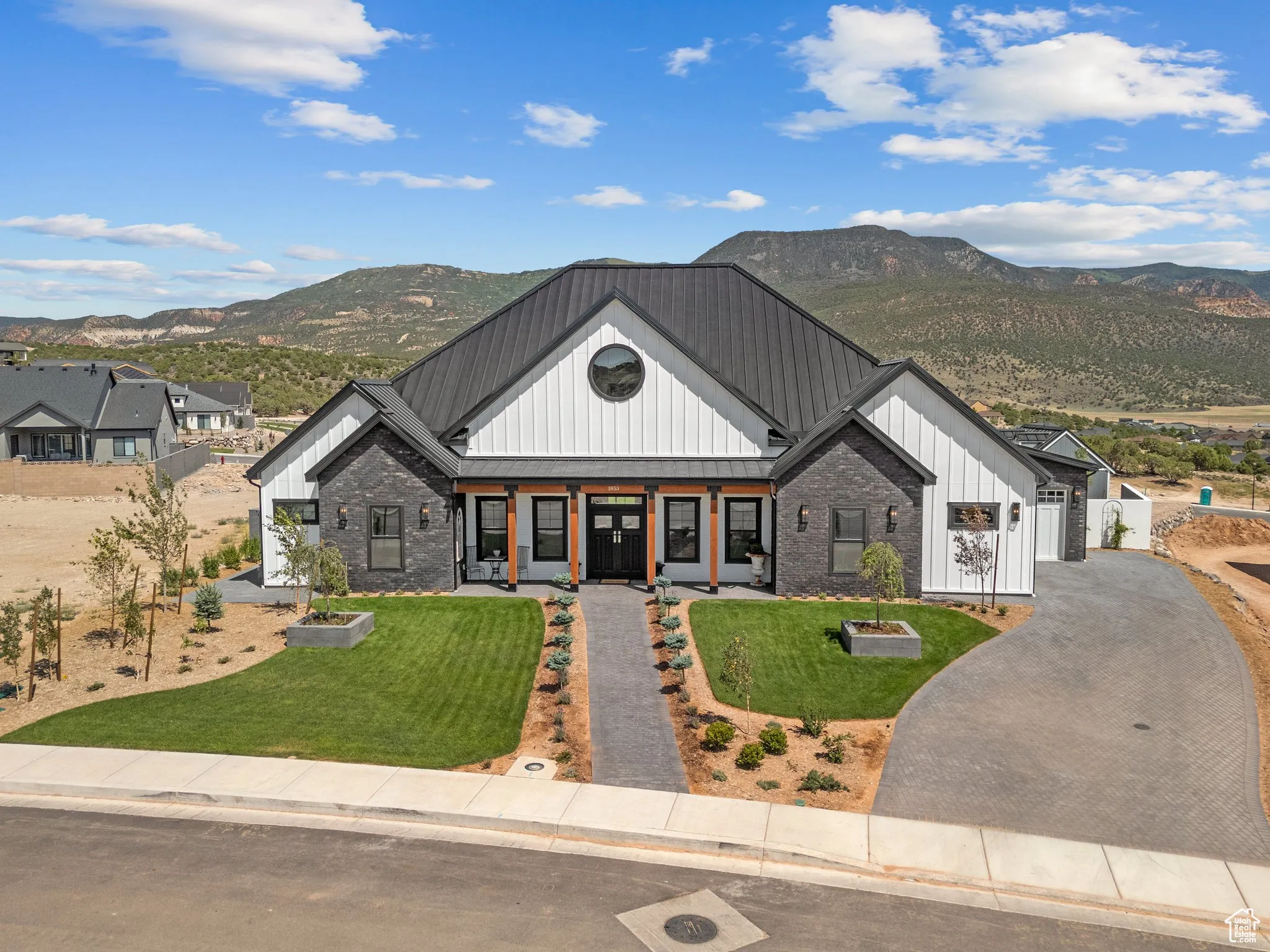 Modern farmhouse style home featuring board and batten siding, a mountain view, a front yard, covered porch, and brick siding
