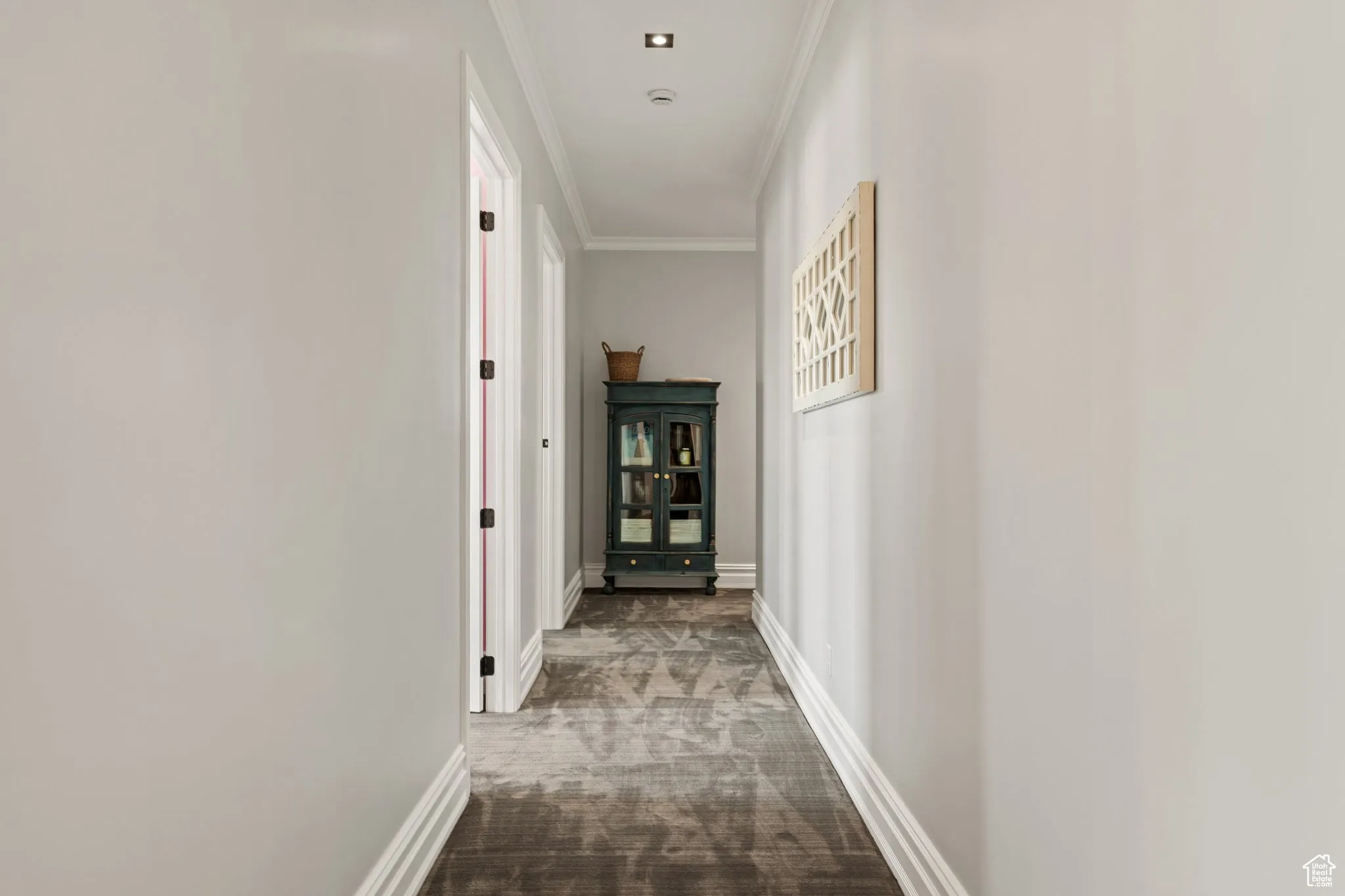 Corridor with ornamental molding and dark colored carpet
