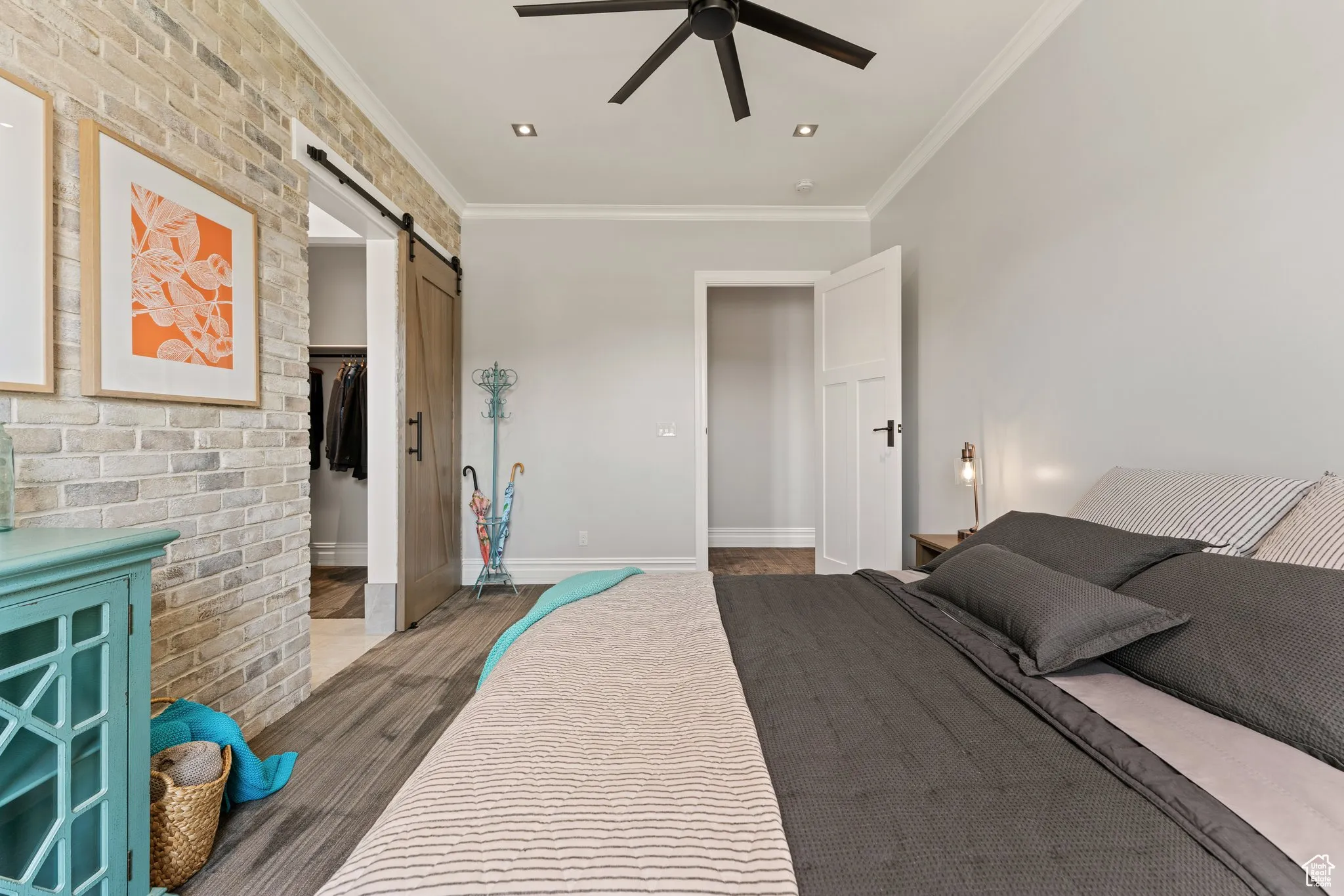 Bedroom featuring a barn door, wood finished floors, ornamental molding, a closet, and a ceiling fan