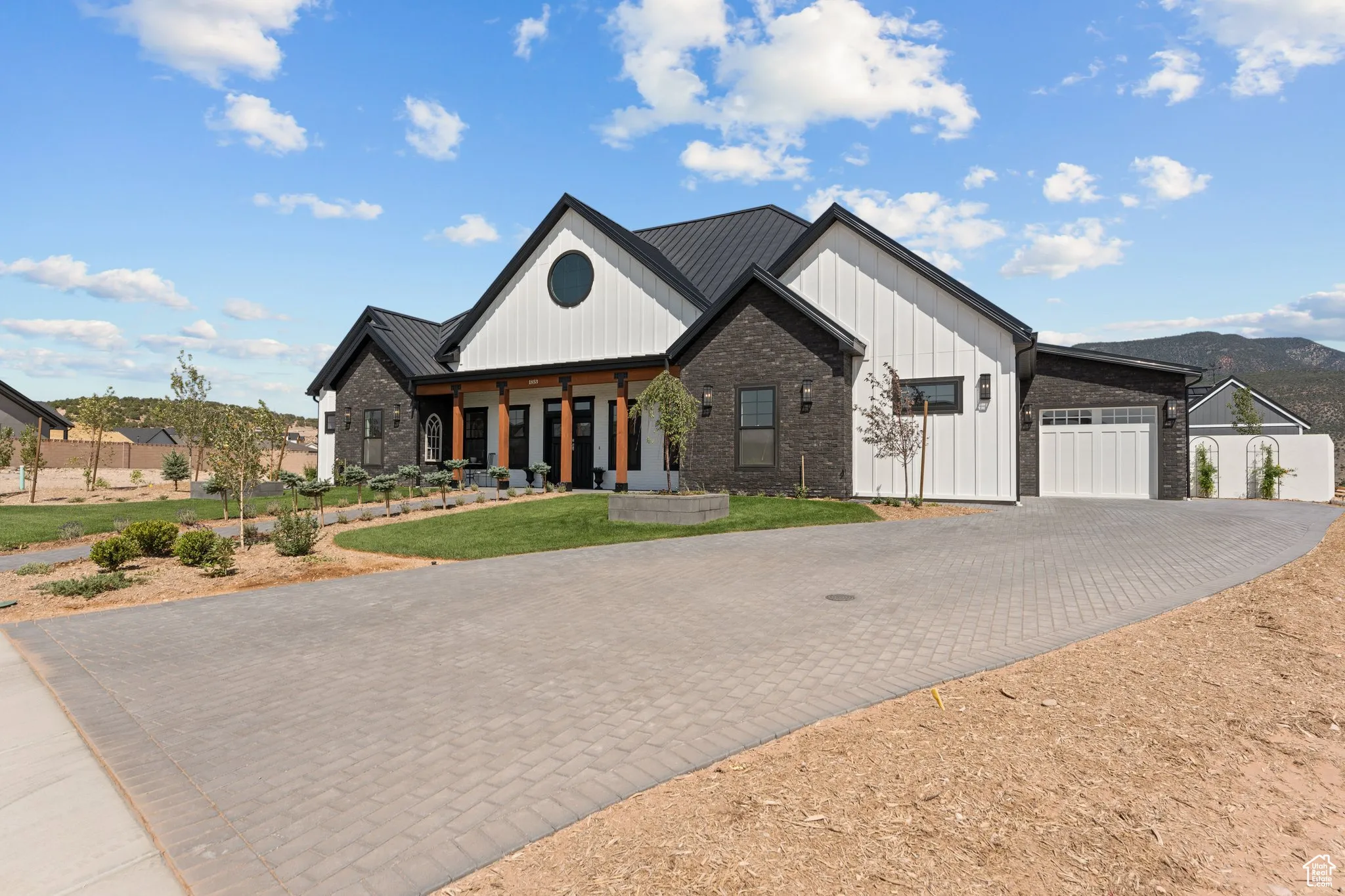 Modern farmhouse style home featuring decorative driveway, an attached garage, board and batten siding, and brick siding