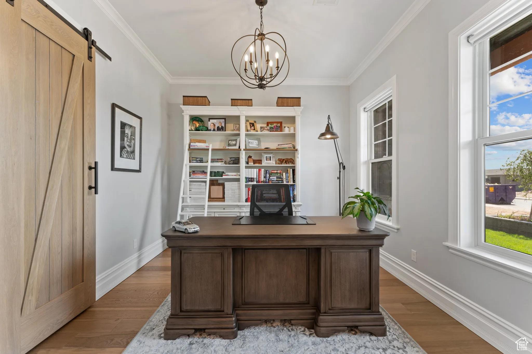 Office space with a barn door, healthy amount of natural light, a chandelier, wood finished floors, and ornamental molding