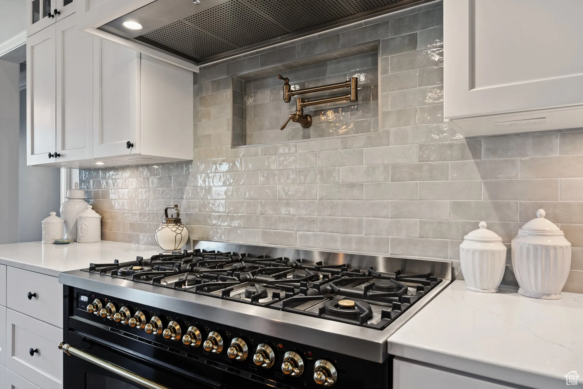Kitchen with stainless steel range with gas cooktop, custom exhaust hood, white cabinets, and backsplash