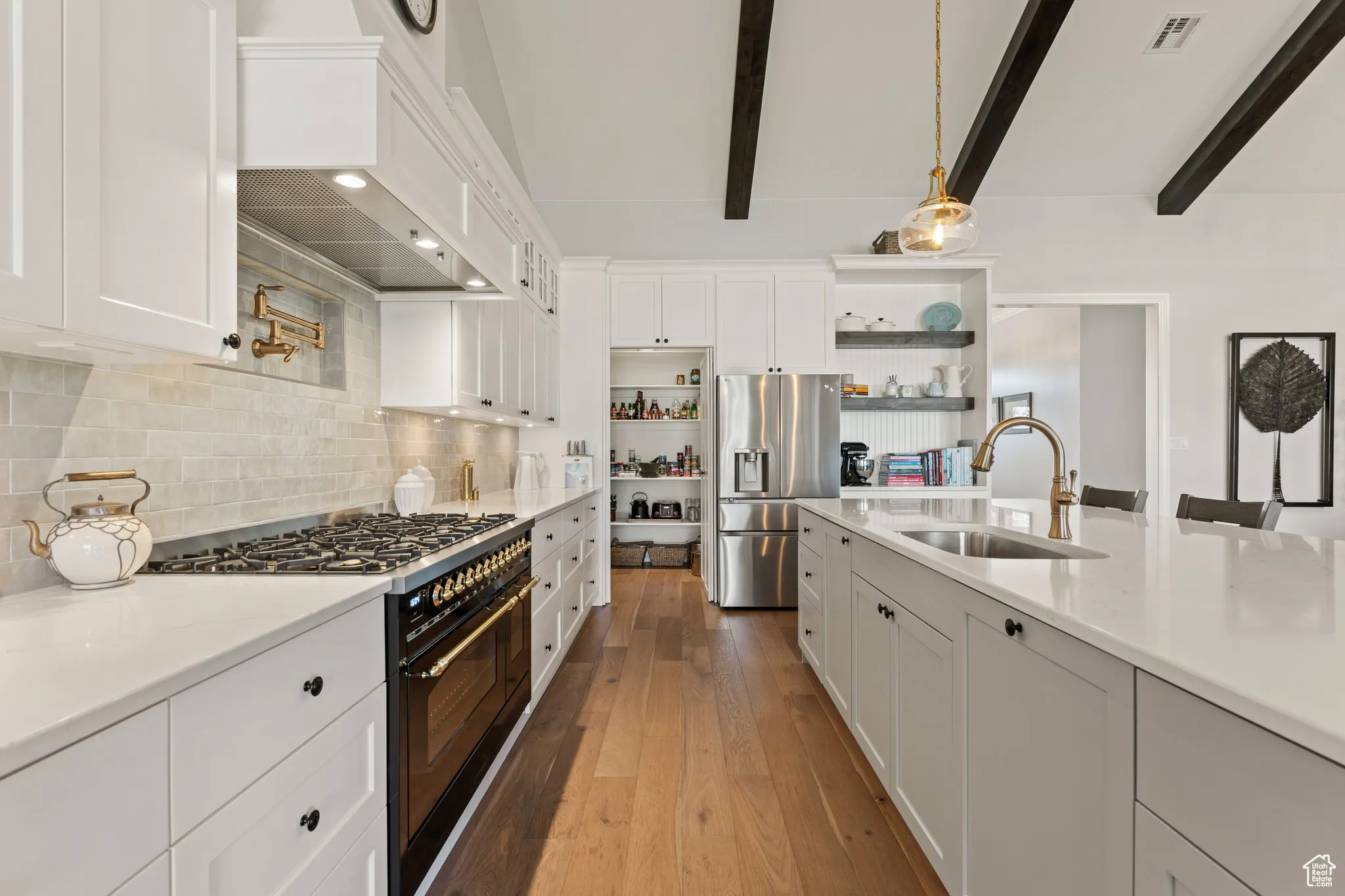Kitchen with double oven range, open shelves, stainless steel fridge with ice dispenser, beamed ceiling, and white cabinetry
