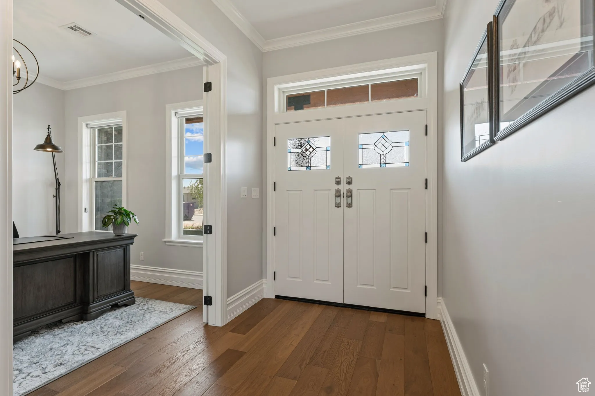 Entrance foyer with dark wood-style floors, crown molding, and a chandelier