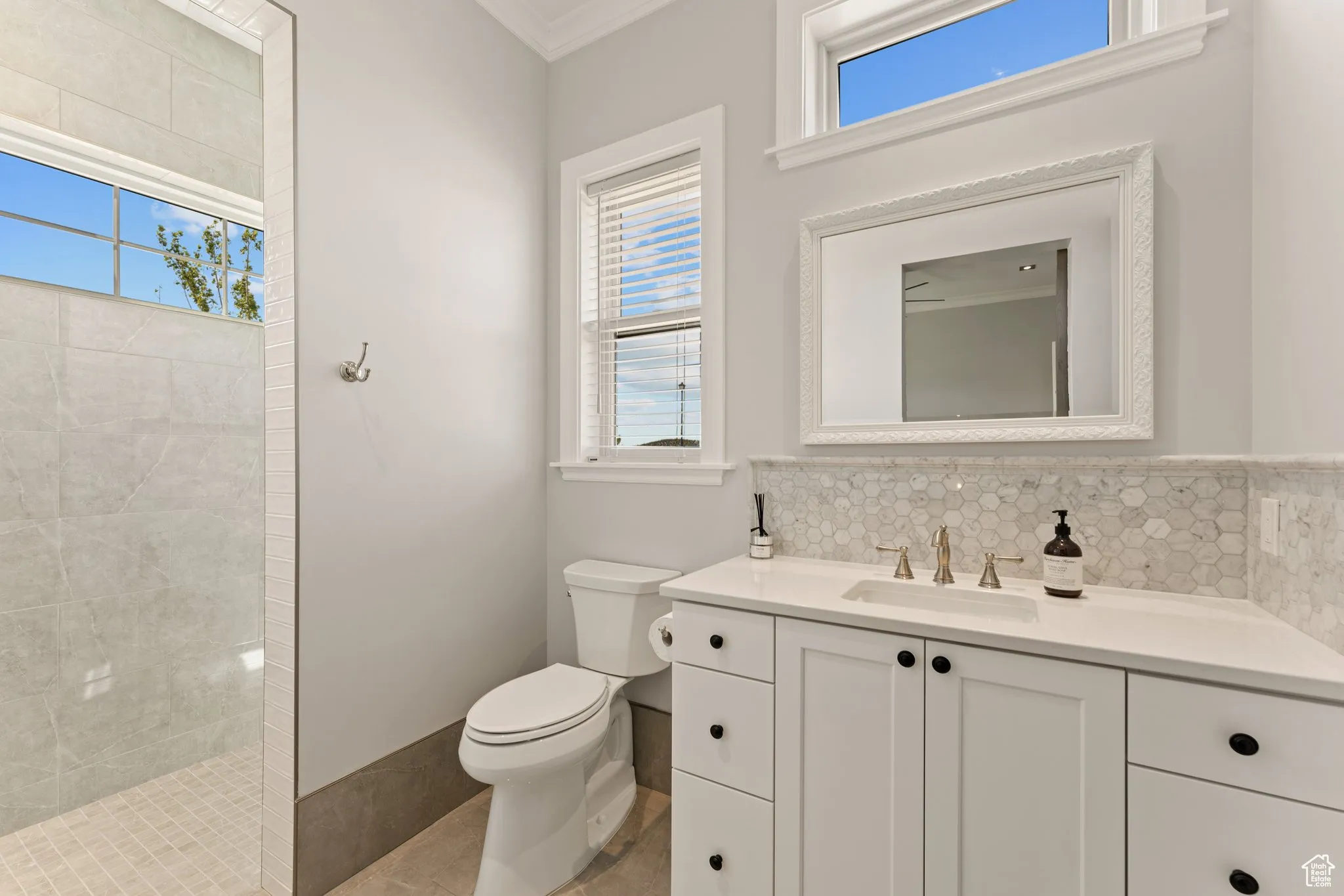 Bathroom featuring vanity, tiled shower, ornamental molding, tasteful backsplash, and tile patterned floors