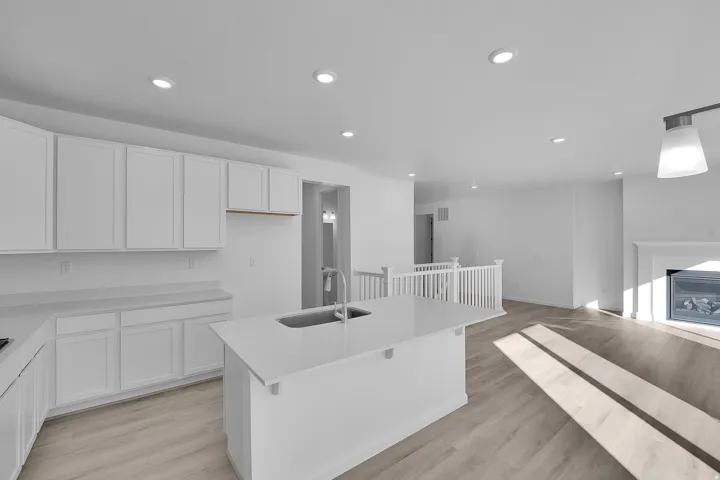 Kitchen with white cabinetry, light wood-type flooring, recessed lighting, a kitchen island with sink, and a glass covered fireplace