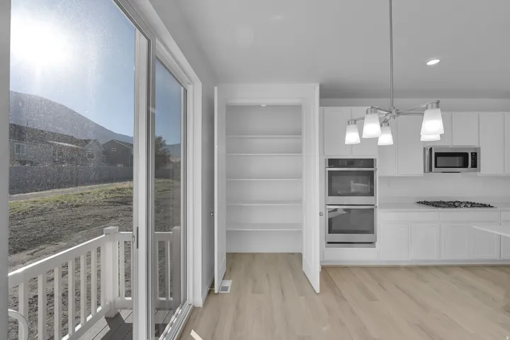 Kitchen with white cabinets, appliances with stainless steel finishes, light wood finished floors, hanging light fixtures, and recessed lighting