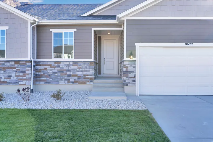 View of exterior entry with an attached garage, stone siding, roof with shingles, and a lawn