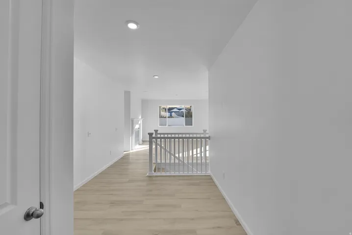 Corridor with an upstairs landing, light wood finished floors, and recessed lighting