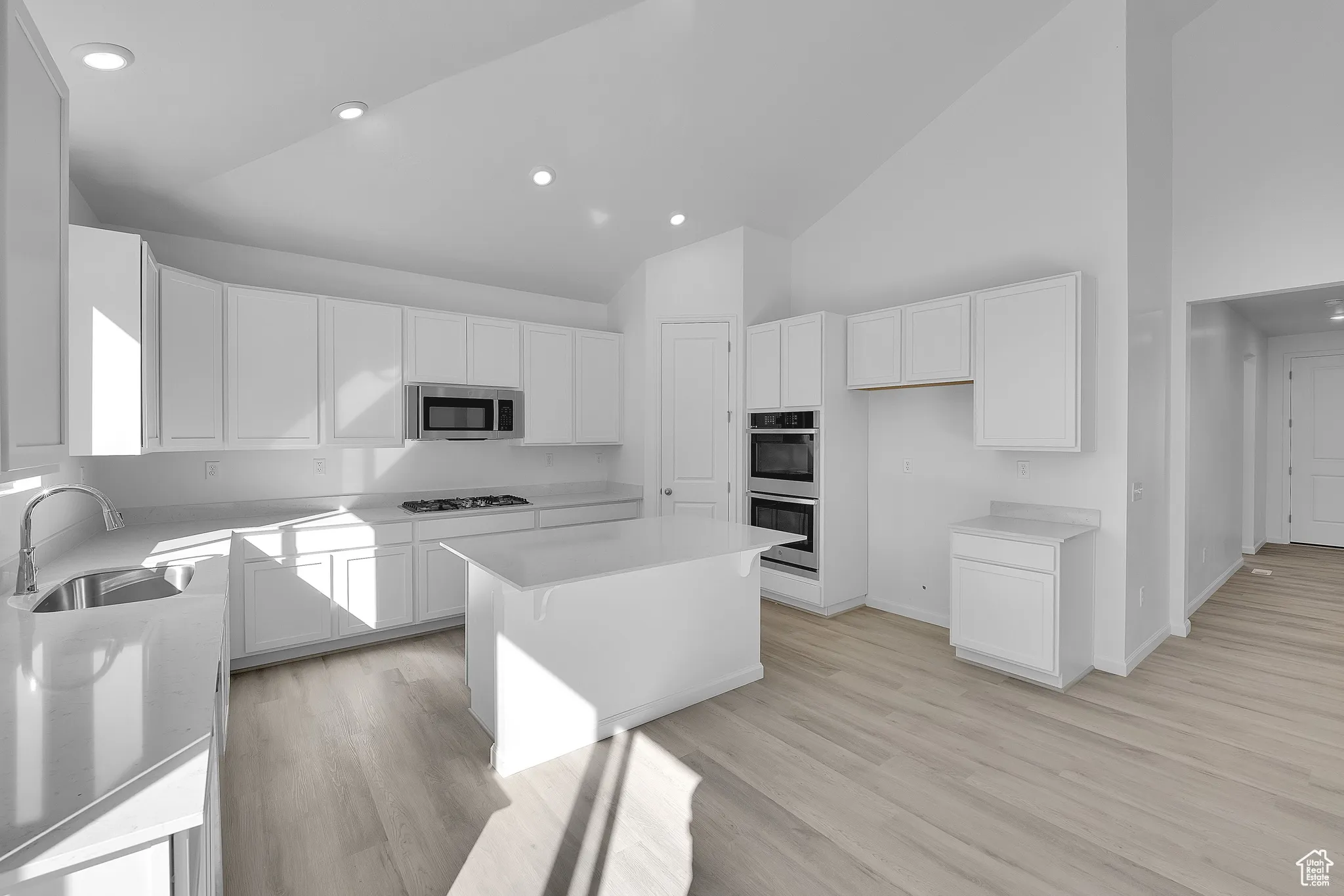 Kitchen with a breakfast bar, a center island, light wood-style flooring, white cabinetry, and high vaulted ceiling
