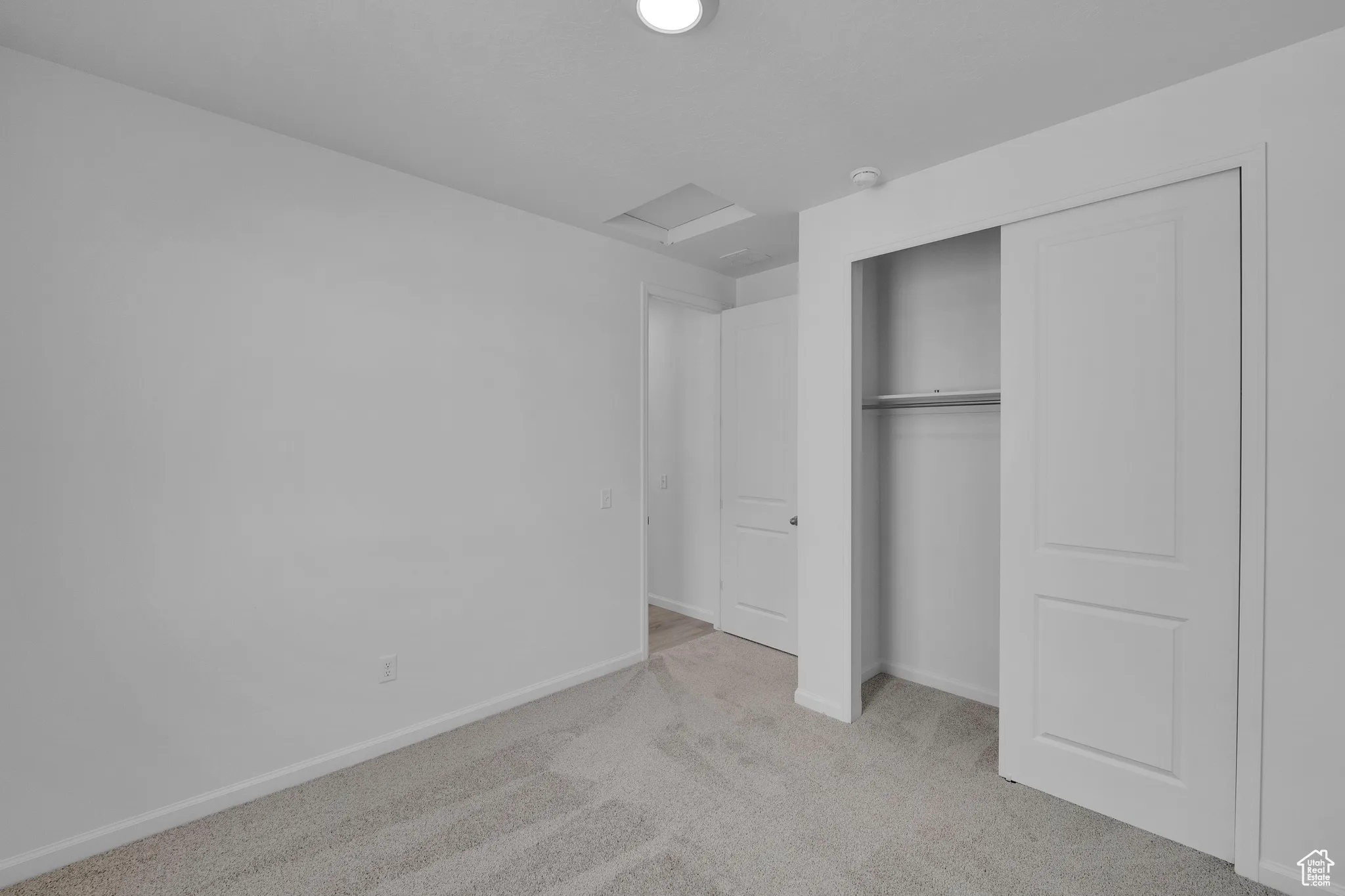 Unfurnished bedroom featuring attic access, light colored carpet, and a closet