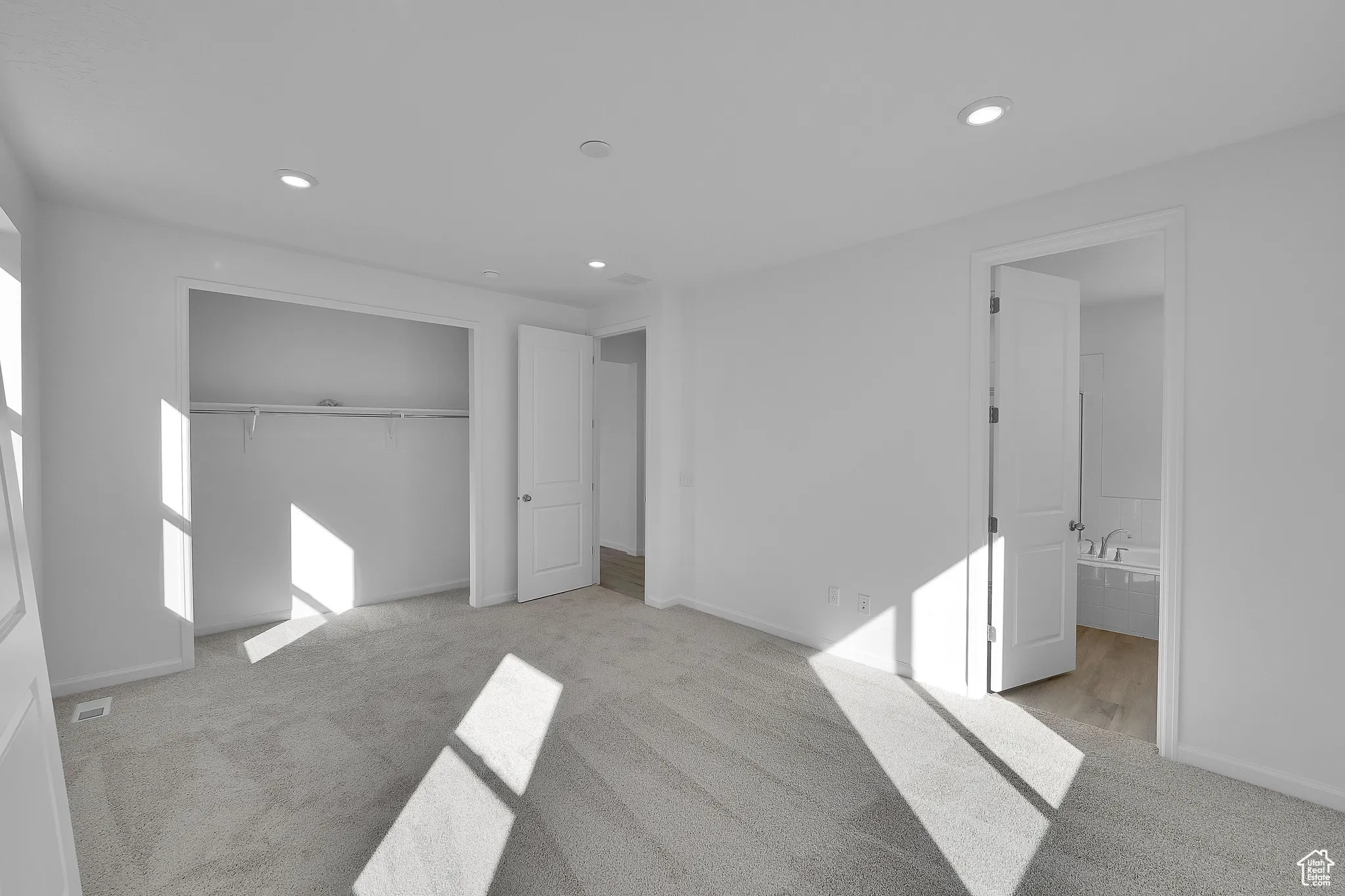Unfurnished bedroom featuring light carpet, recessed lighting, ensuite bathroom, and a closet
