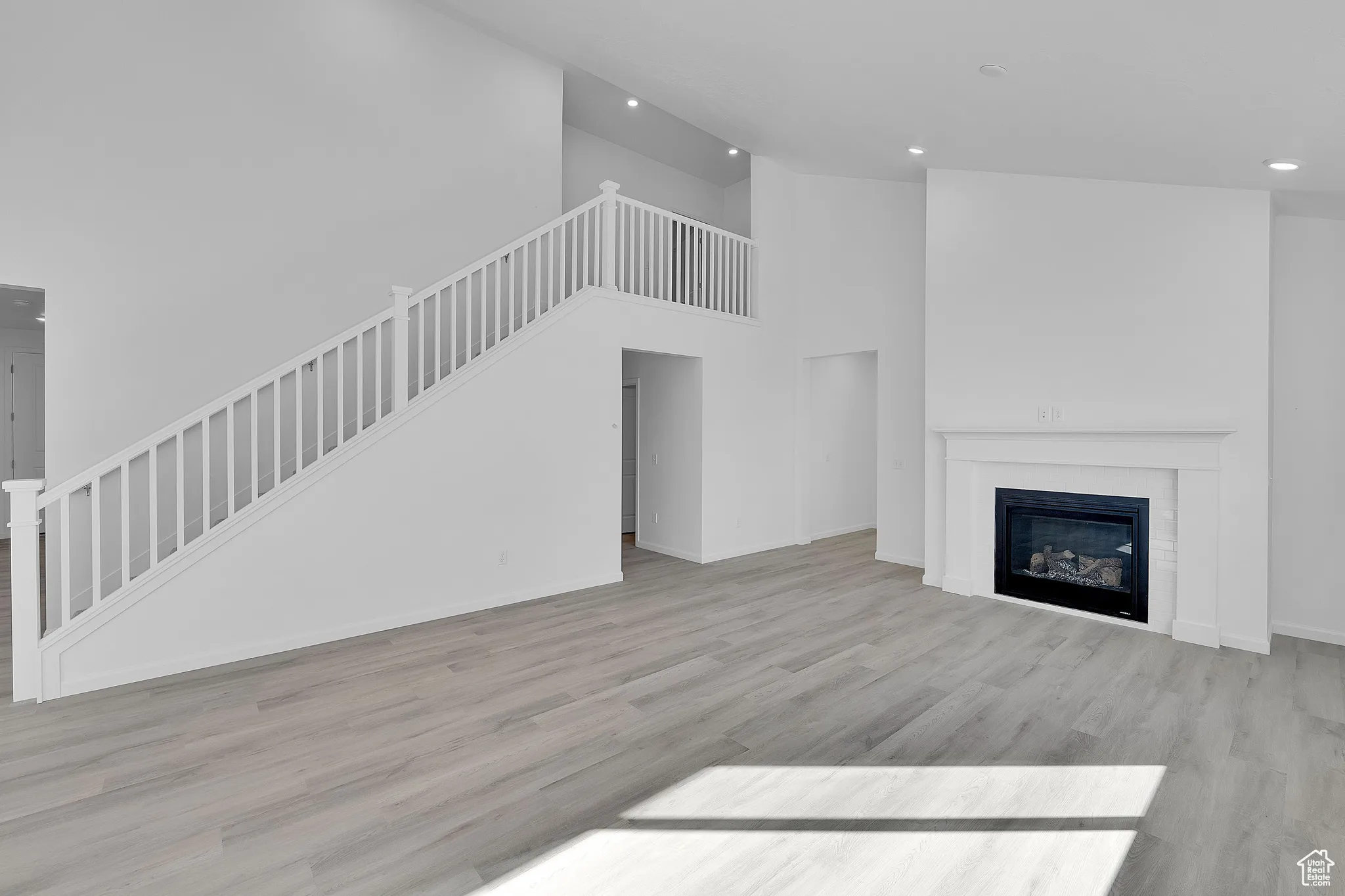 Unfurnished living room with a high ceiling, light wood finished floors, stairway, a glass covered fireplace, and recessed lighting