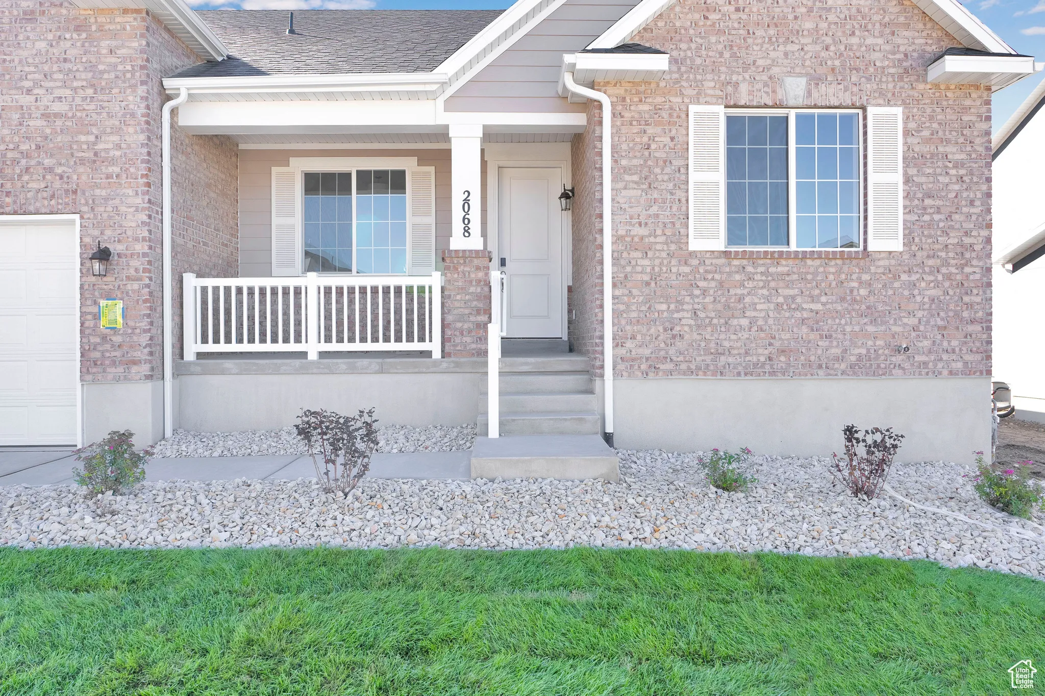 Property entrance featuring covered porch, brick siding, and a garage