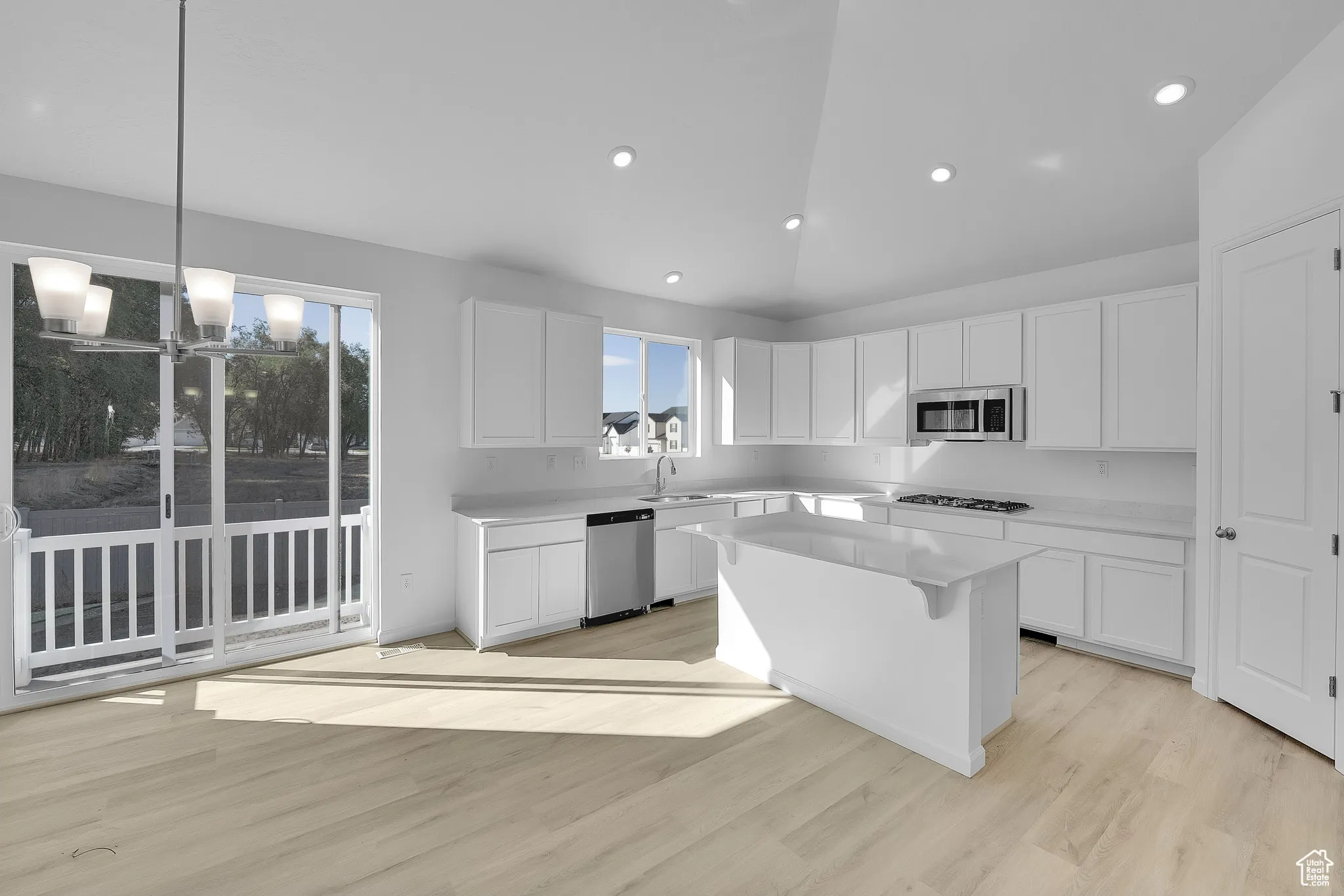 Kitchen with decorative light fixtures, light wood-type flooring, white cabinetry, a kitchen island, and plenty of natural light