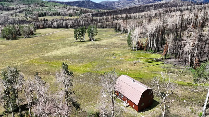 Spacious natural landscape featuring a single barn-style structure with a brown metal roof, set amidst open fields and distant forested hills