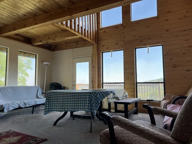 Open-concept room featuring a wood plank ceiling and exposed beams