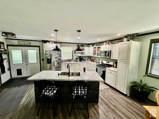 Kitchen with appliances with stainless steel finishes, dark wood-style flooring, white cabinets, decorative light fixtures, and a kitchen bar
