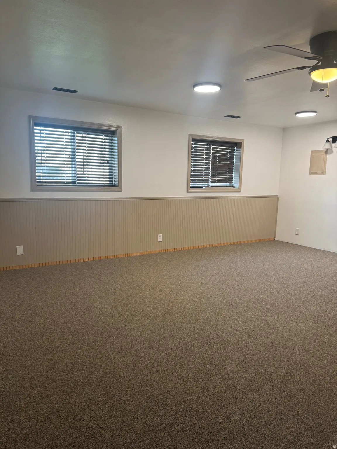 Carpeted spare room featuring a wainscoted wall and ceiling fan