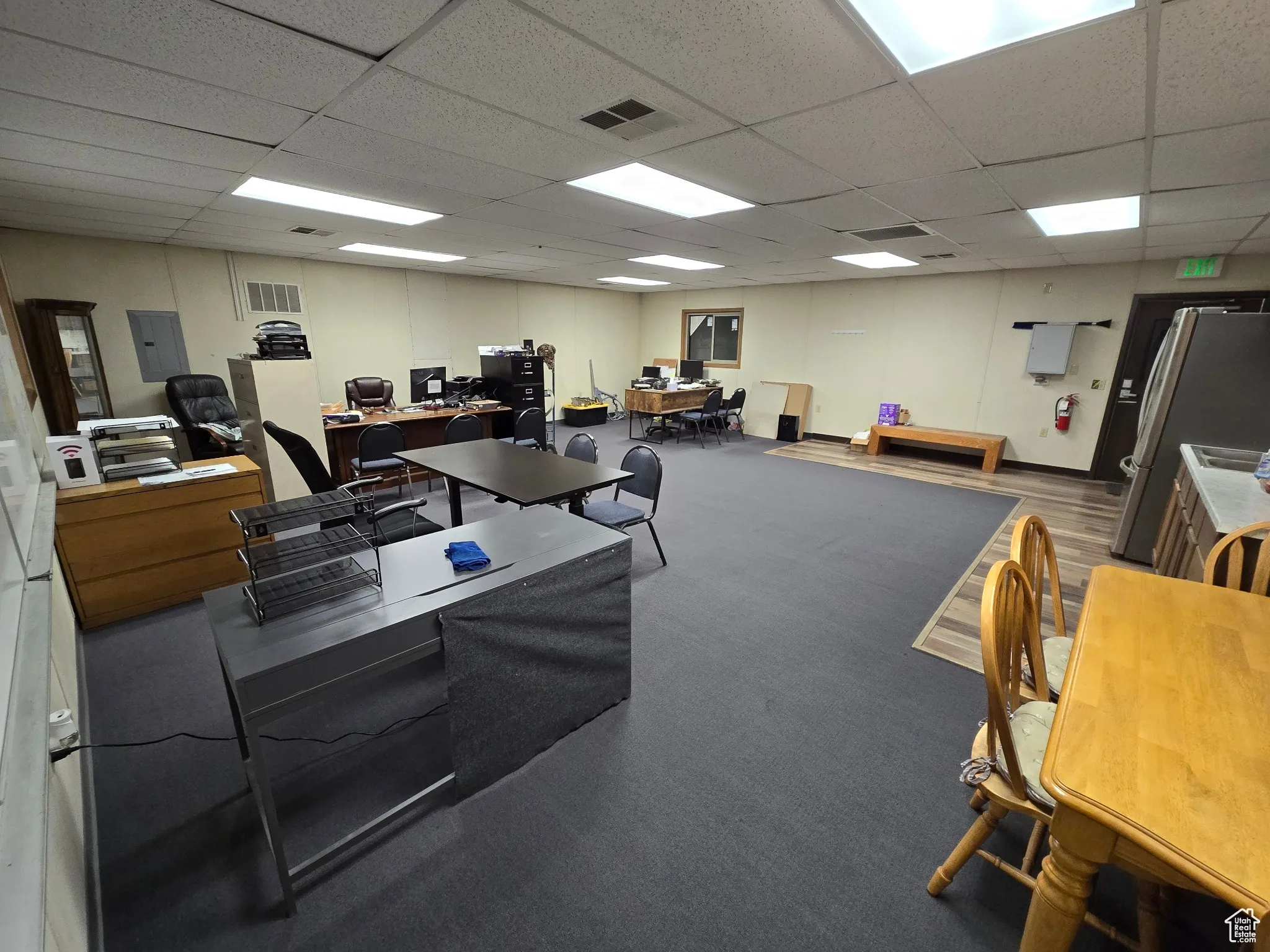 Carpeted home office with a drop ceiling and electric panel