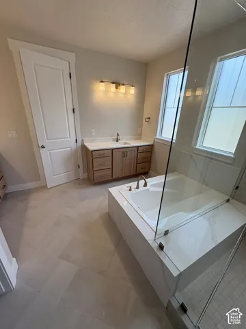 Dual vanity with wood-finish cabinetry, built-in soaking tub, and glass shower enclosure