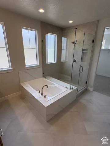 Soaking tub with bronze-finish fixtures, a glass-enclosed shower with subway tile, and light-colored tile flooring