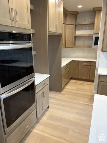 Stainless steel double wall ovens, wood-finish flooring, white countertops, built-in microwave, and light wood cabinetry