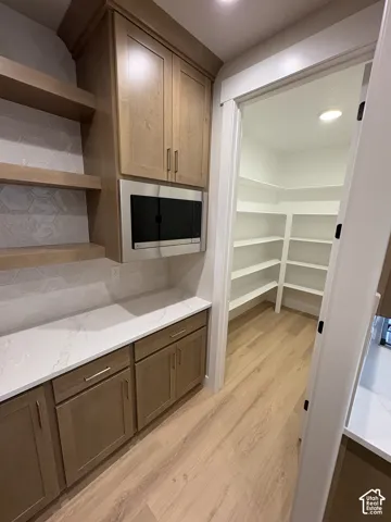 Built-in cabinetry with wood-finish doors, stainless steel microwave, and open shelving
